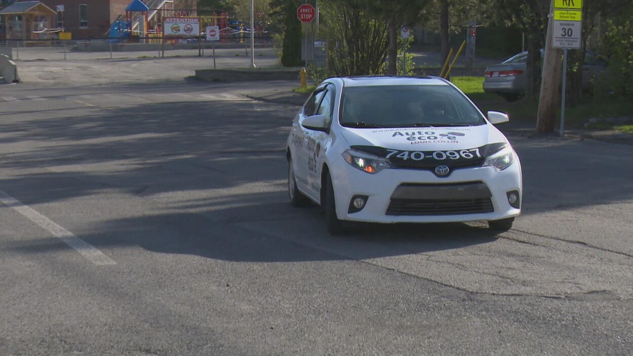 Une voiture portant de logo de l'école de conduite entre dans un stationnement.