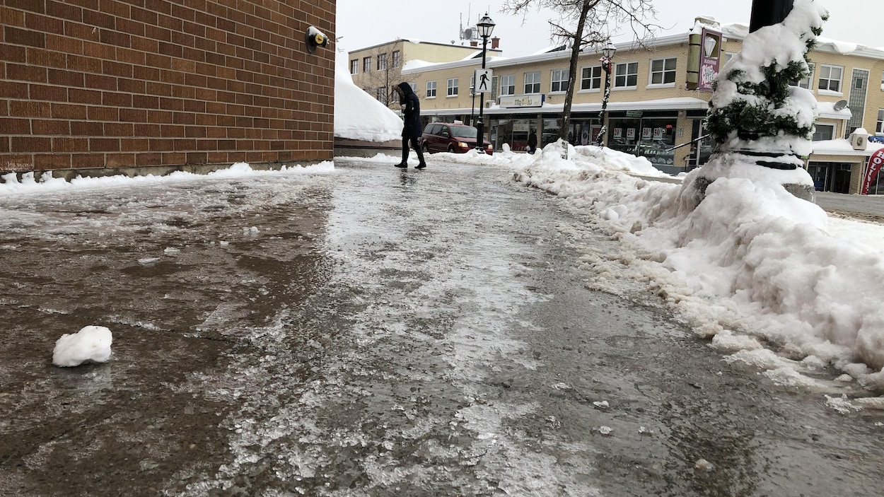 Une femme marche difficilement sur un trottoir recouvert de verglas