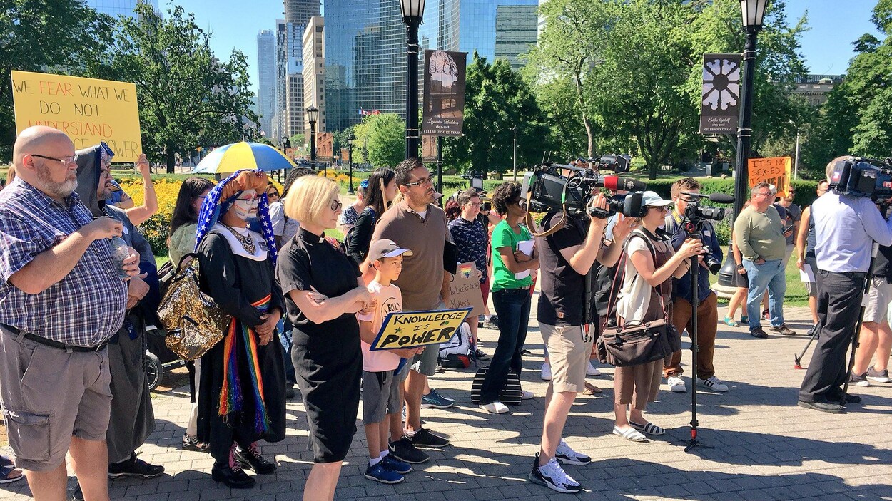 un groupe de personne portant des pancartes rassemblées devant Queen's Park. un groupe de personne portant des pancartes rassemblées devant Queen's Park.