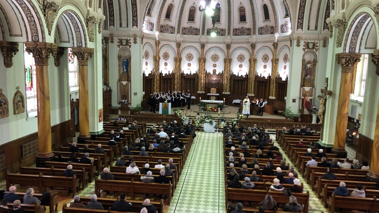 Des dizaines de personnes assises sur des bancs dans une église lors de funérailles.