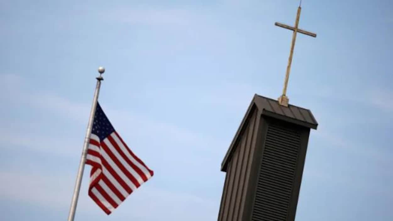 le drapeau des états-unis flotte dans les airs à côté de la croix de l'église cahtolique
