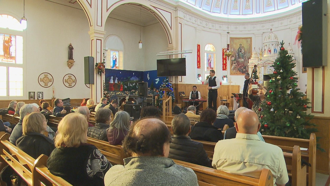 Gens assis dans l'église avec un chanteur et un sapin de Noël.