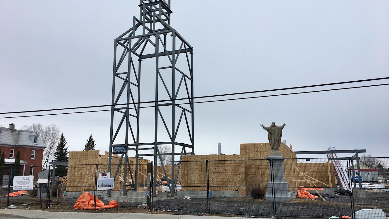 Chantier de construction où se dresse le châssis en acier d'un clocher et une statue de Jésus.