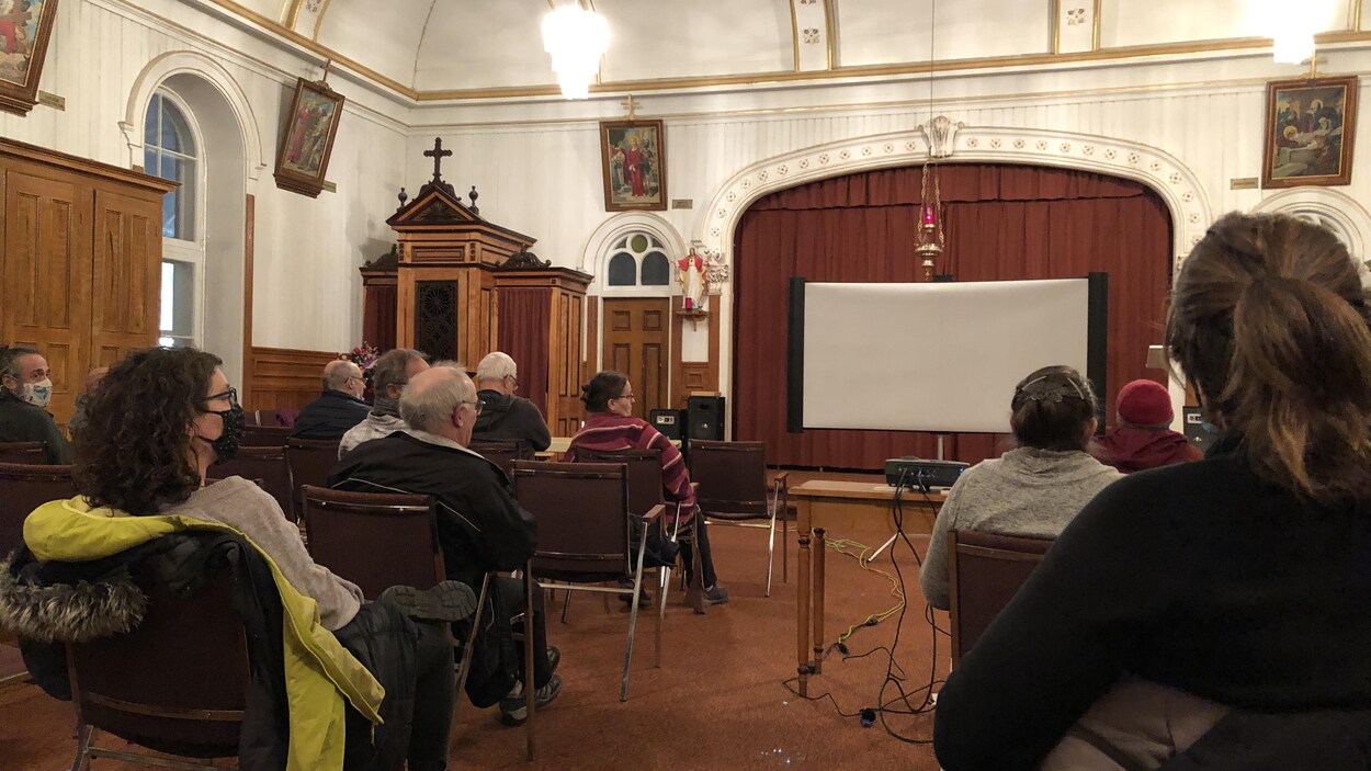 Des gens assis devant un écran dans la sacristie de l'église de Saint-Ulric.