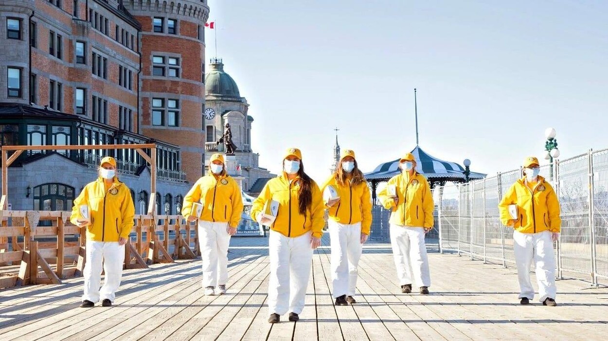 Des membres de l'Église de Scientologie qui portent des manteaux jaunes et des masques sur la terrasse Dufferin à Québec.