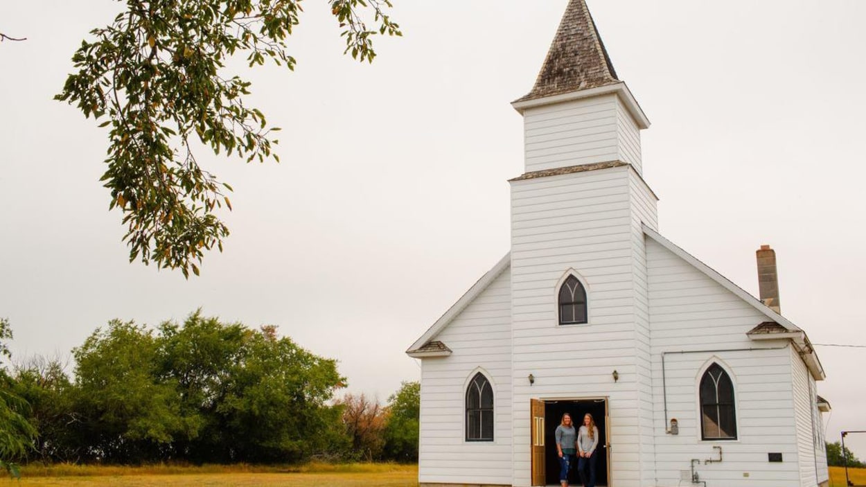 Deux femmes sur le perron d'une petite église blanche, sur un terrain vague.