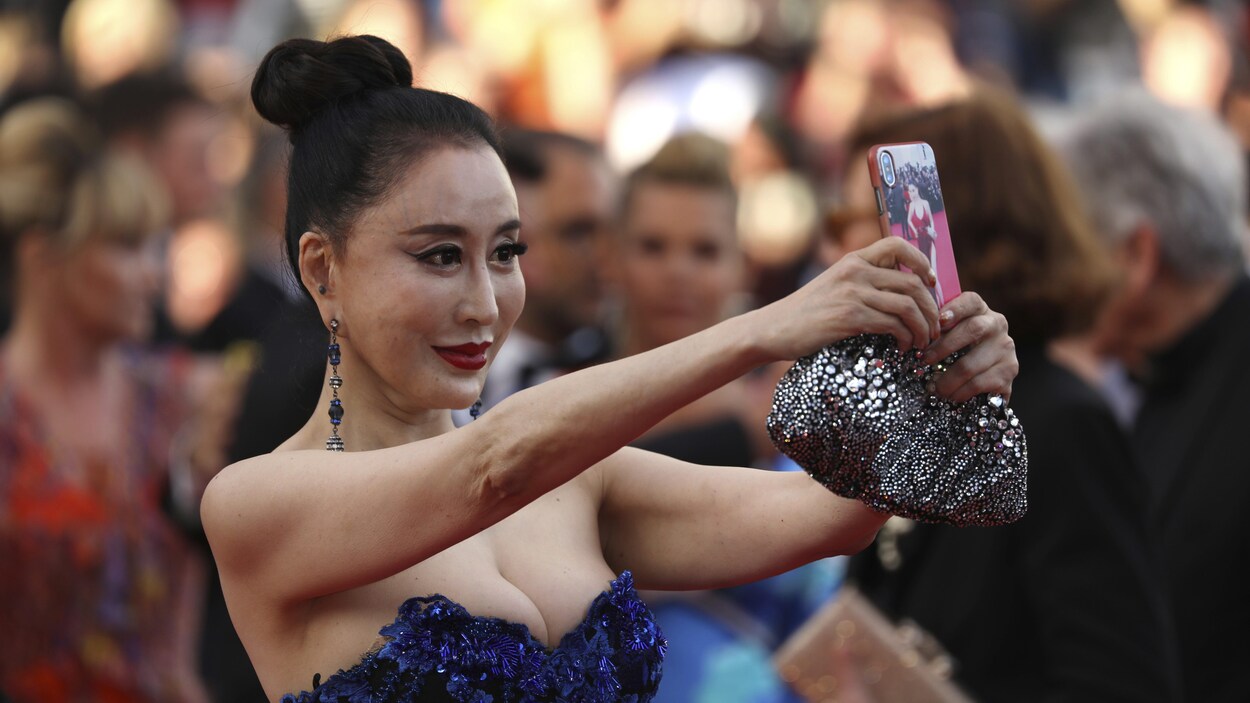 Une femme vêtue d'une robe élégante prend un égoportrait à son arrivée à la cérémonie d'ouverture du Festival de Cannes.