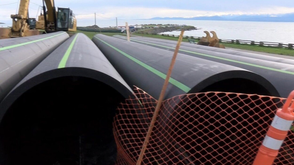 Gros plan sur des tuyaux couchés sur le sol avec une grue et l'océan en arrière-plan