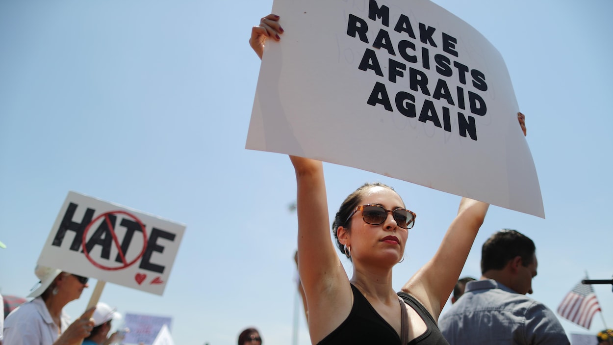 Une femme tient une affiche sur laquelle est écrit : « Make racists afraid again ».