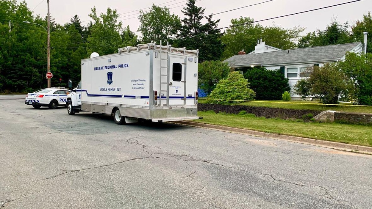 Un camion et un véhicule de police sont stationnés devant une maison cachée derrière des buissons.