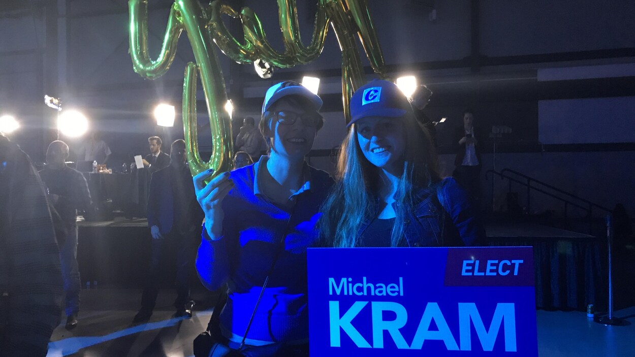 Deux jeunes femmes, toutes de bleu vêtues, posent face à l'objectif. Elles ont le sourire aux lèvres. L'une d'elles tient dans ses mains une pancarte du candidat conservateur Michael Kram, l'autre arbore un ballon doré.