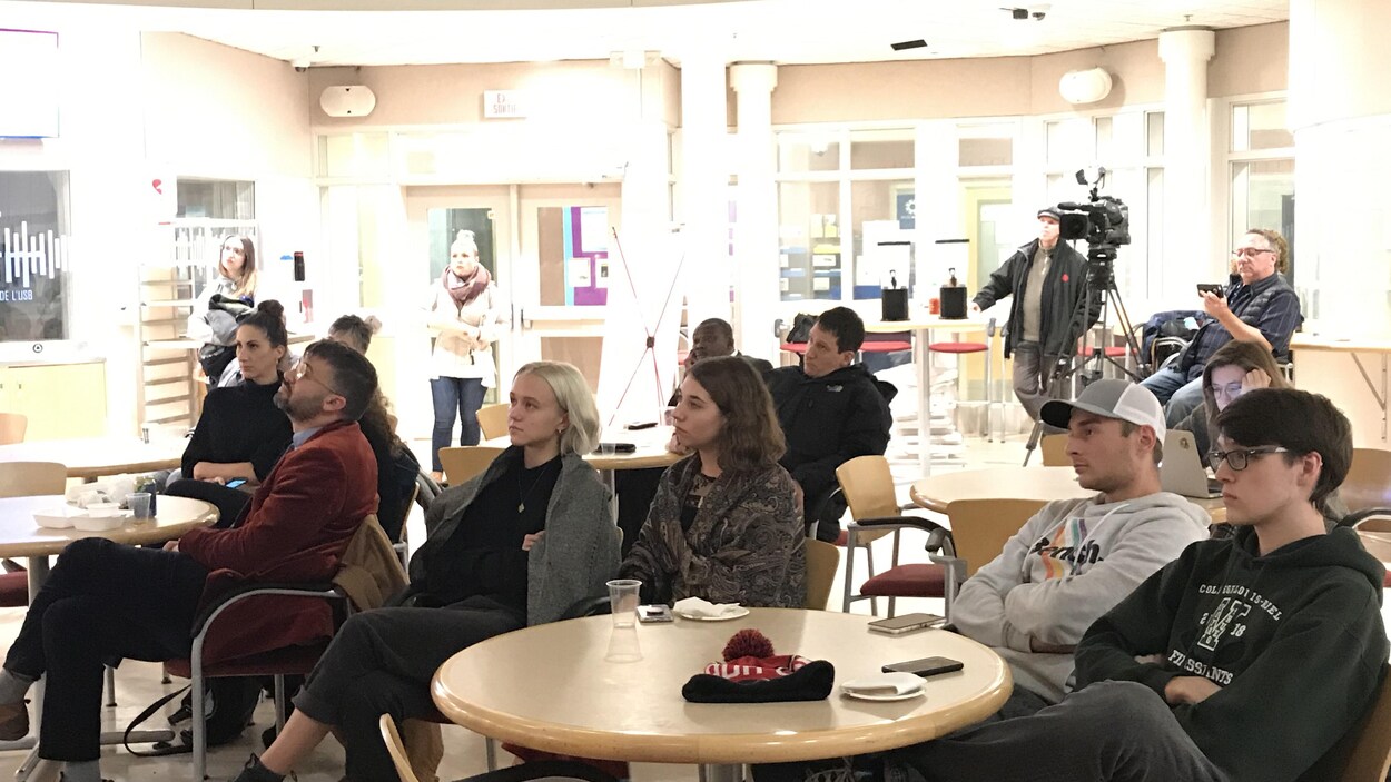 Des gens assis autour d'une table regardent la retransmission d'un débat.