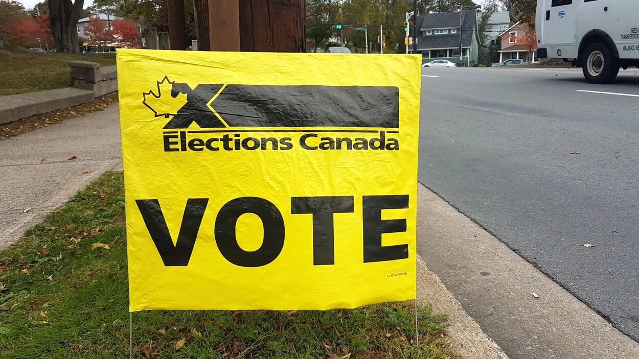 Le mot « VOTE » en grosses lettres sur une affiche jaune d'Élections Canada plantée dans le gazon.