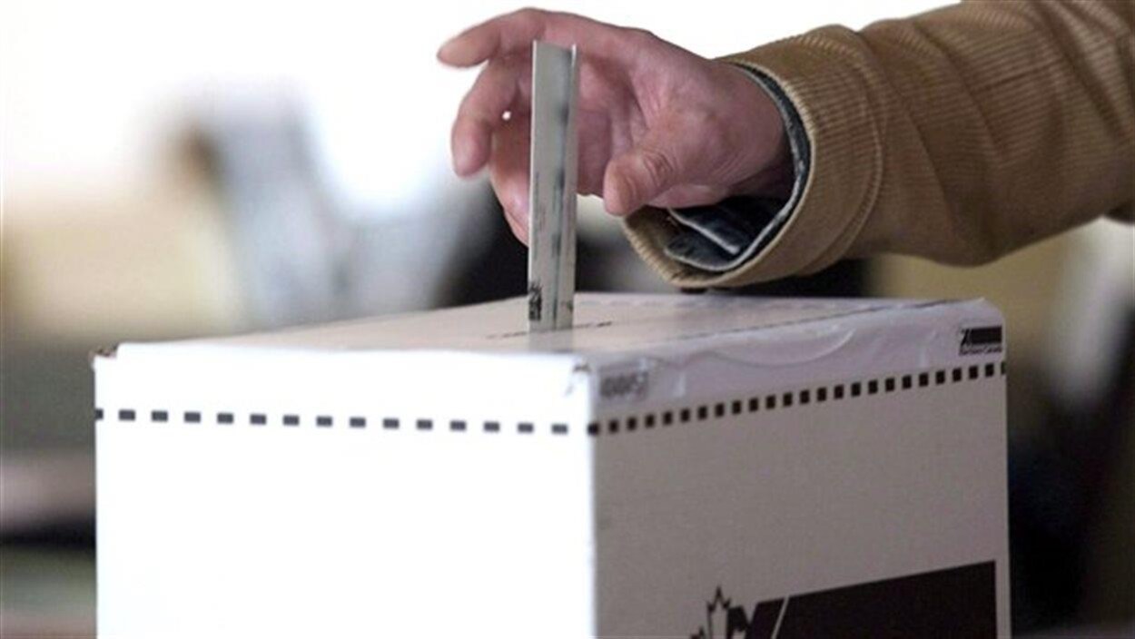 Un homme glisse un bulletin de vote dans une boîte de scrutin.