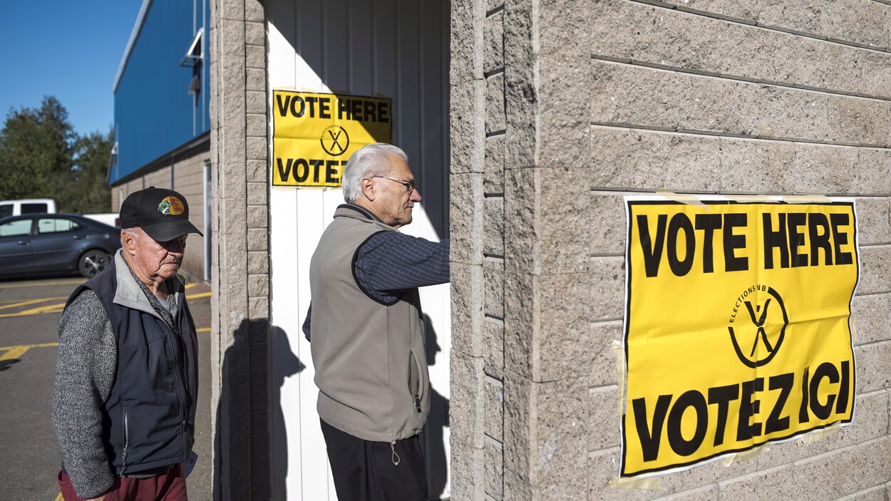 Deux hommes entrent dans un bâtiment sur lequel il est écrit : « Vote here, votez ici ».