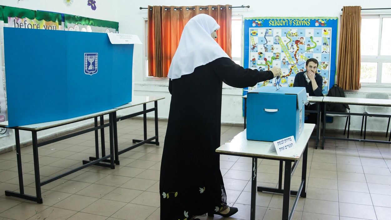Une femme portant le voile dépose son bulletin de vote dans l'urne, sous le regard d'un observateur.
