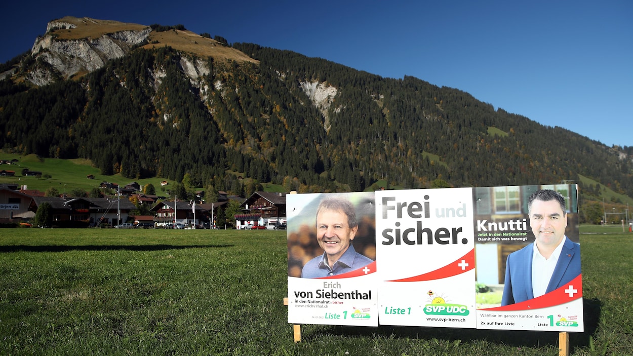 Des affiches électorales devant un pré et une colline.