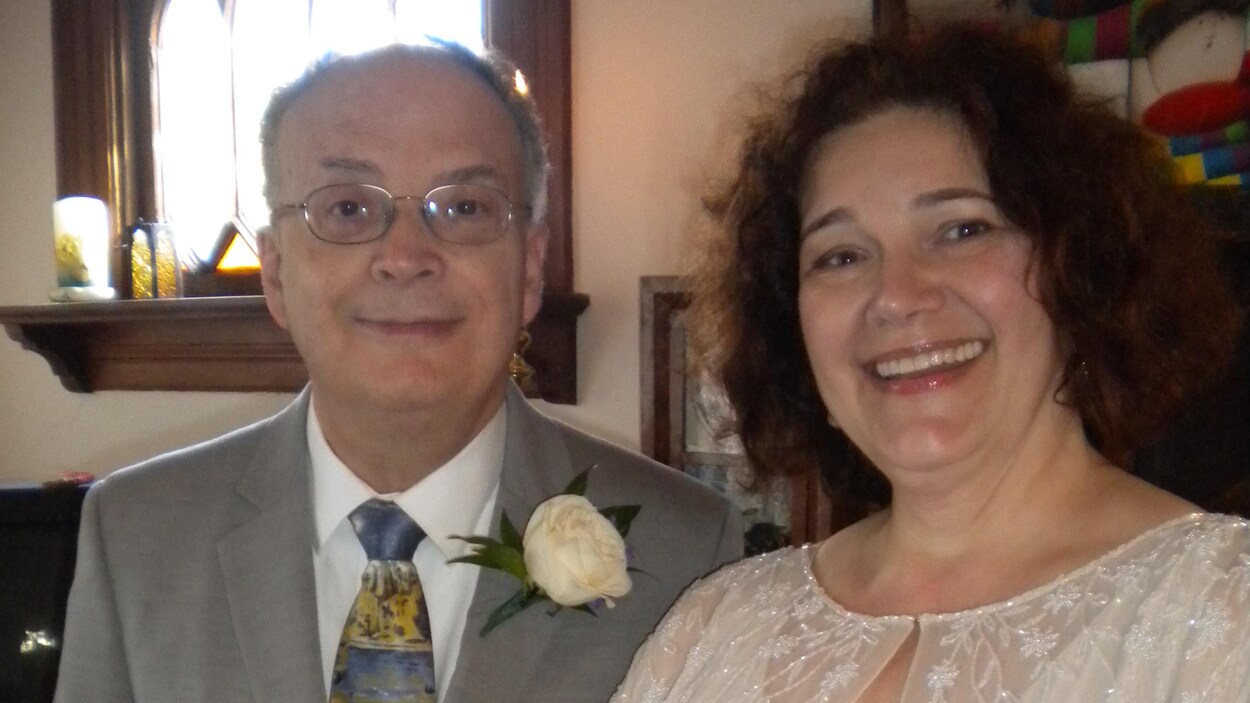Une femme habillée en blanc avec un bouquet pose à côté d'un homme le jour de leur mariage.