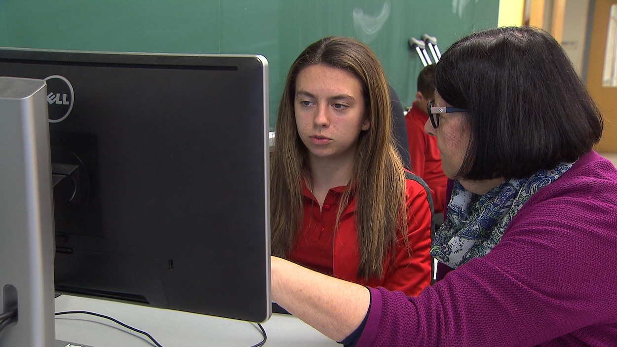 Une enseignante aide une élève qui écrit à l'ordinateur.