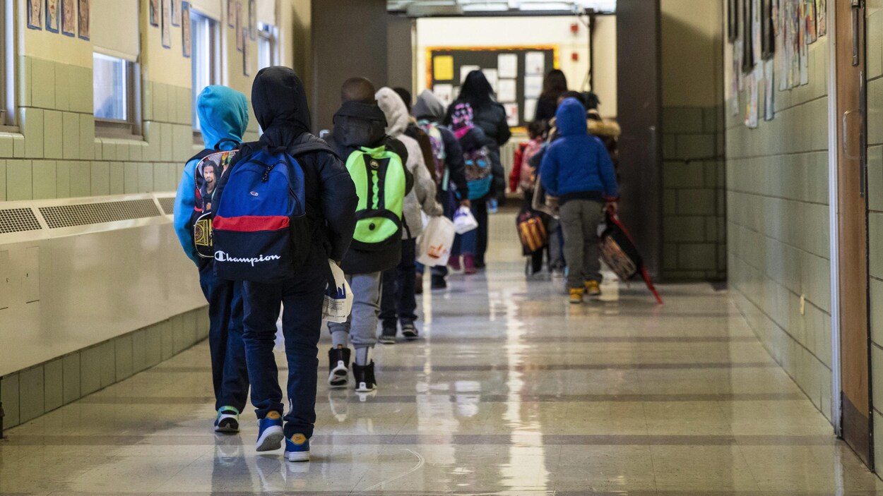 Des élèves vus de dos marchent dans un couloir au moment de leur arrivée à l'école.