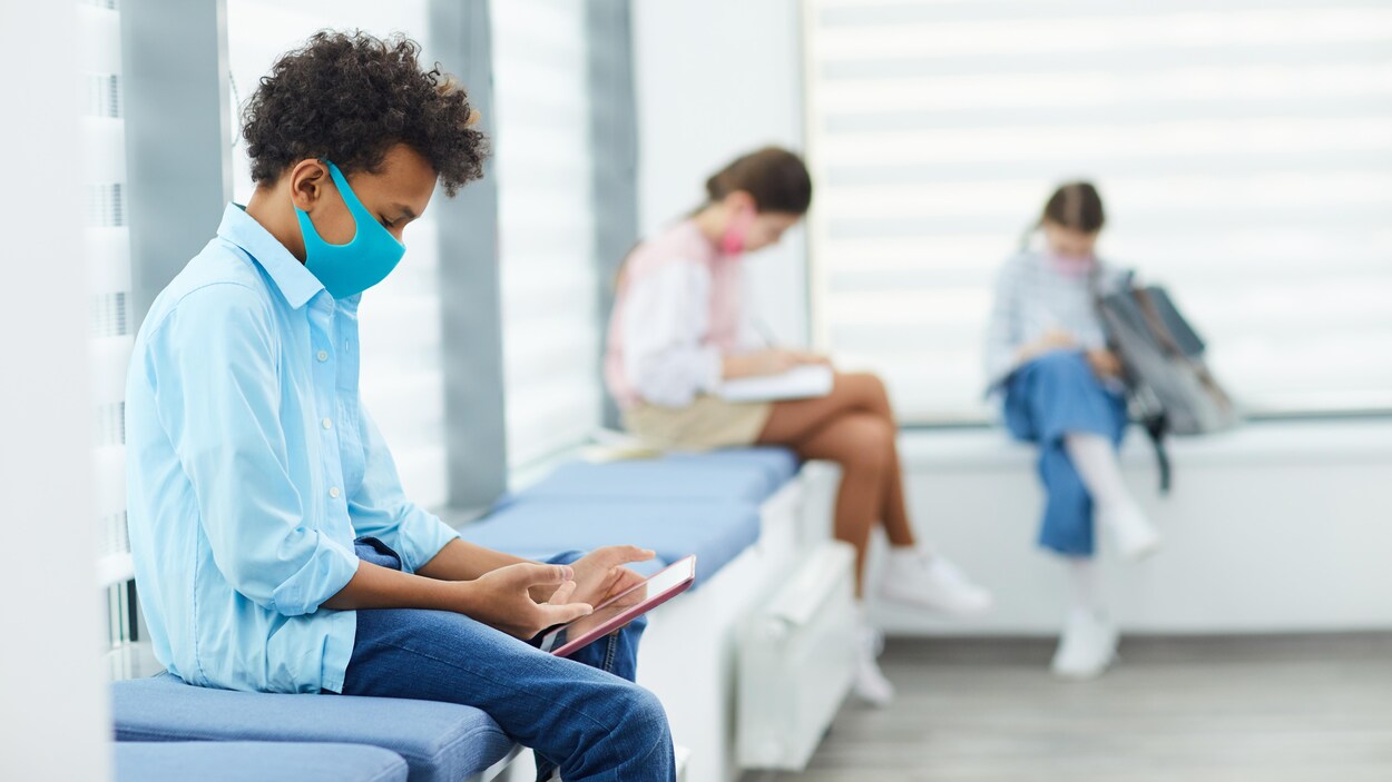 Des élèves qui portent des masques et sont assis loin les uns des autres consultent leur tablette.