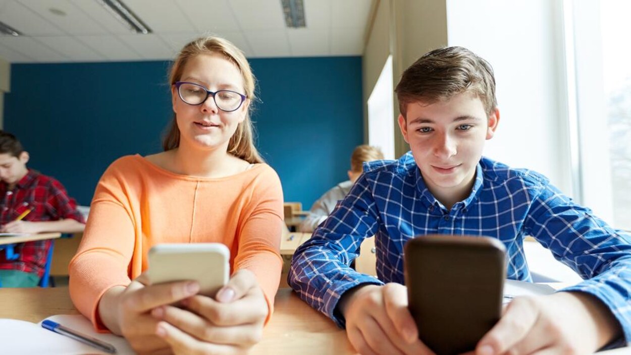 Des élèves consultent leur téléphone en classe. Des élèves consultent leur téléphone en classe.