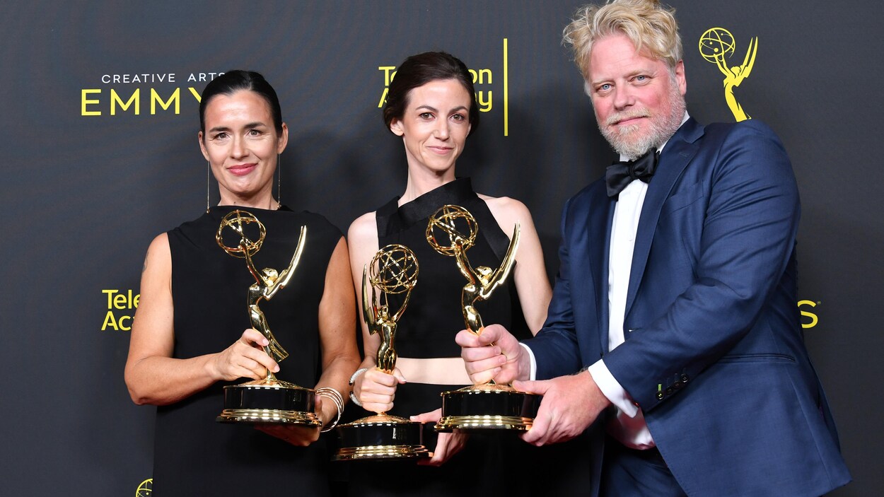 Les trois personnes sourient et ont chacune une statuette en main.