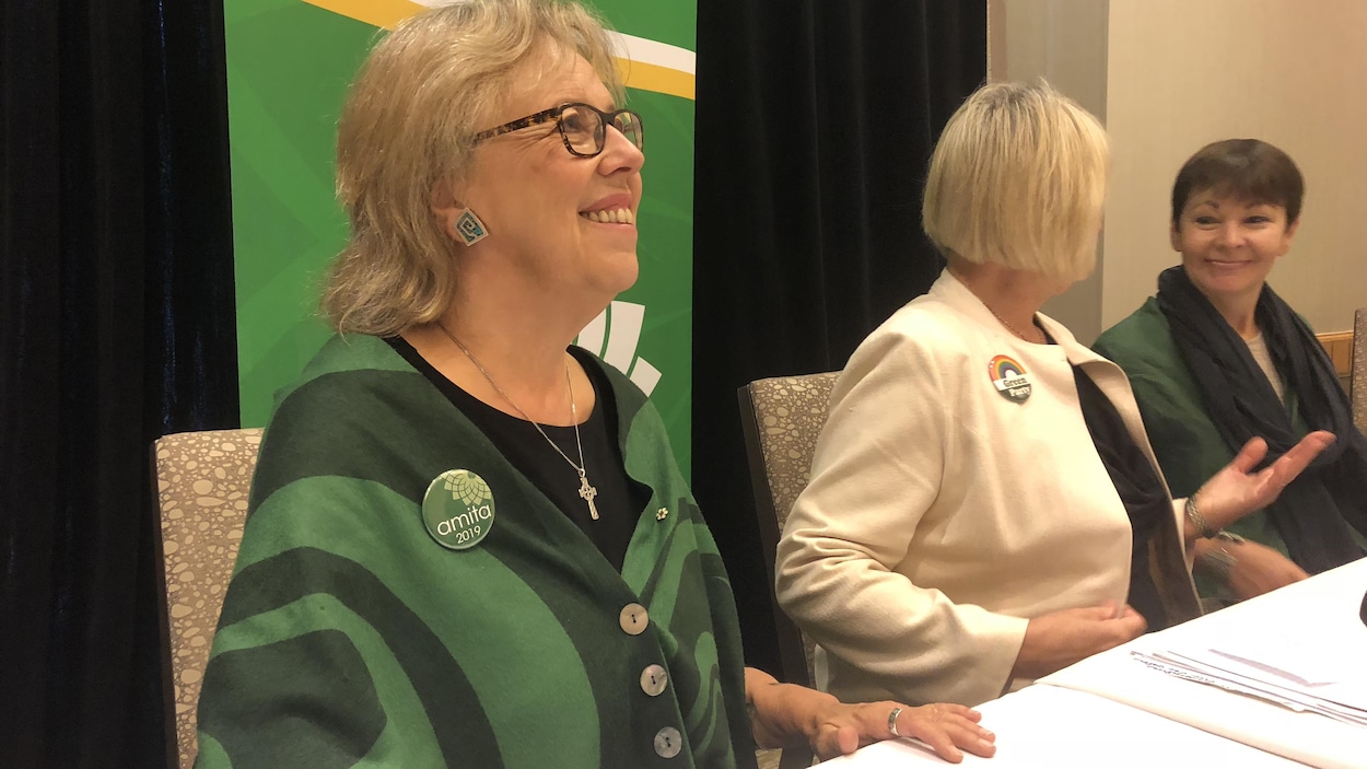Trois femmes assises sur autour d'une table dont une regarde droit devant elle en train de sourire.