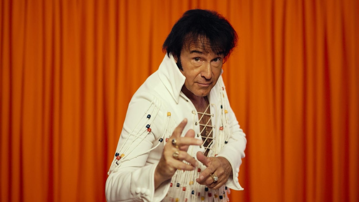 Un homme avec les cheveux noirs porte un costume blanc à franges.