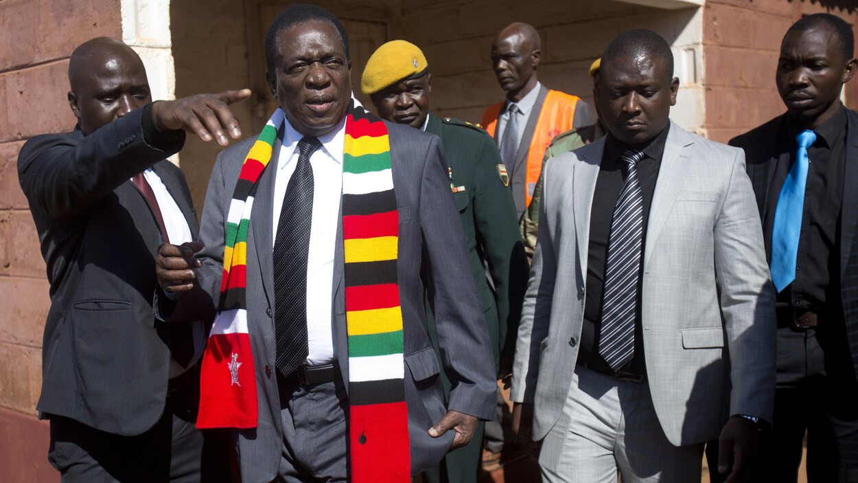 Portant une écharpe aux couleurs nationales, Emerson Mnangagwa marche aux côtés de membres de sa garde rapprochée.