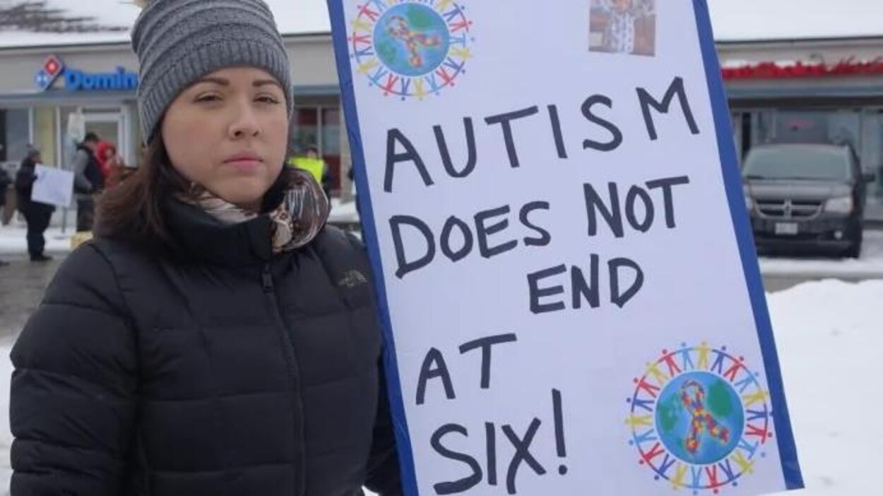 Emily Sheridan à l'extérieur. Elle tient une pancarte sur laquelle on peut lire « Autism Does Not End At Six! »