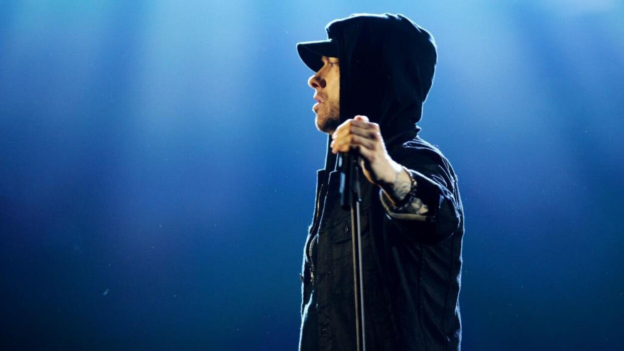 Eminem porte un vêtement à capuche et tient un micro dans la main droite.