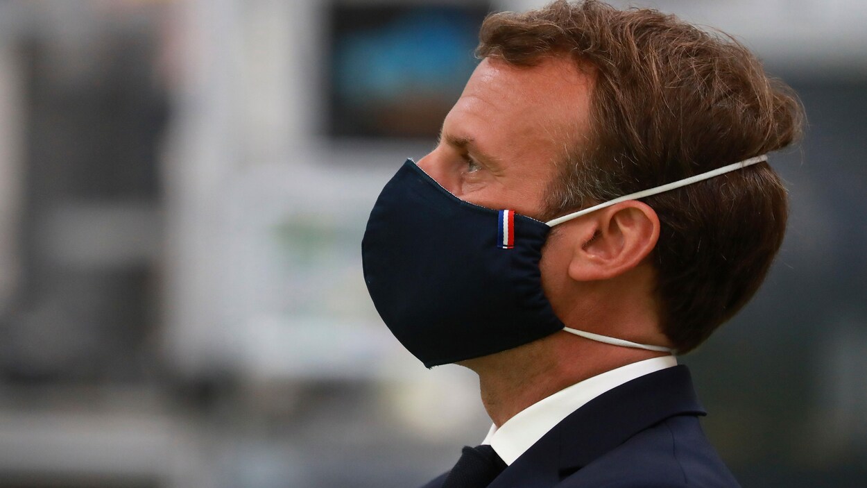 M. Macron vu de profil, portant un masque de couleur bleu marin.