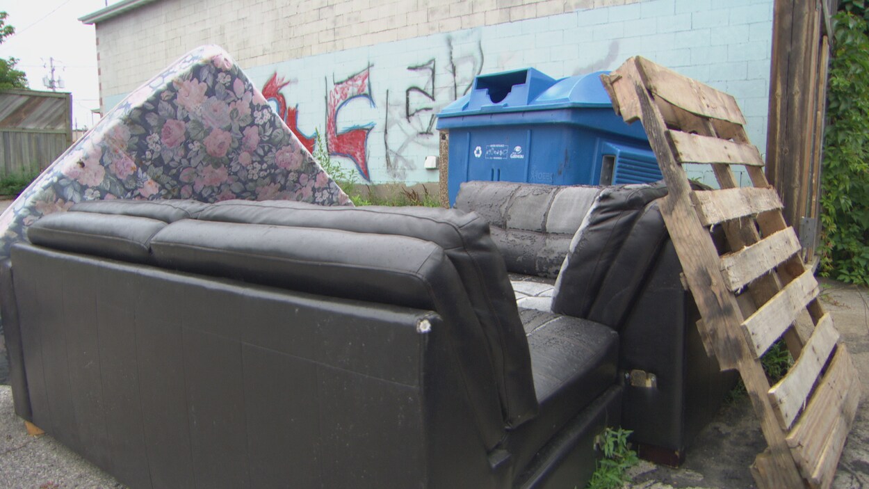 Un matelas, un vieux canapé et une structure de bois près d'un bac de recyclage bleu.