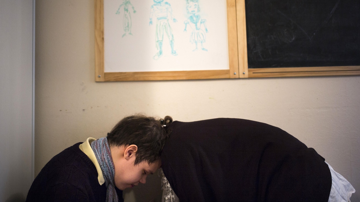 Un jeune garçon autiste se confie à une intervenante, sous un tableau rempli de dessins montrant des héros et des princesses.