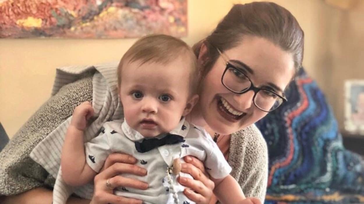 Jillian Schneider est assise sur un divan avec un bébé dans les bras.