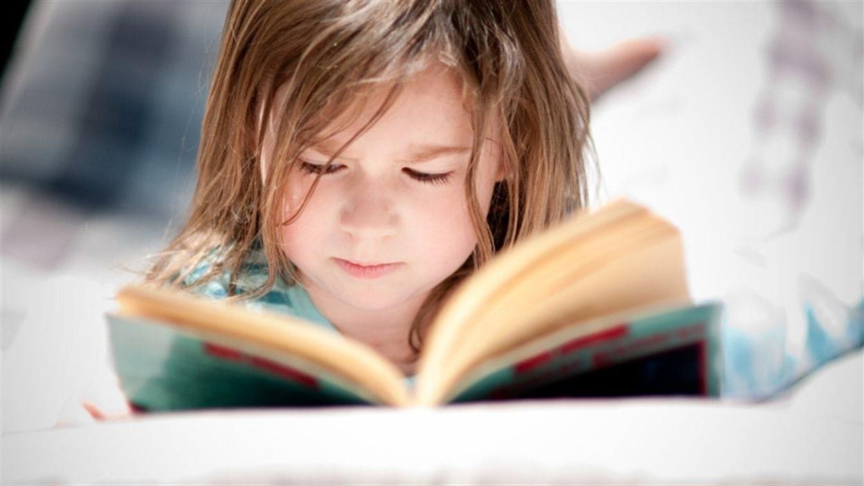 Un enfant allongé lit un livre.