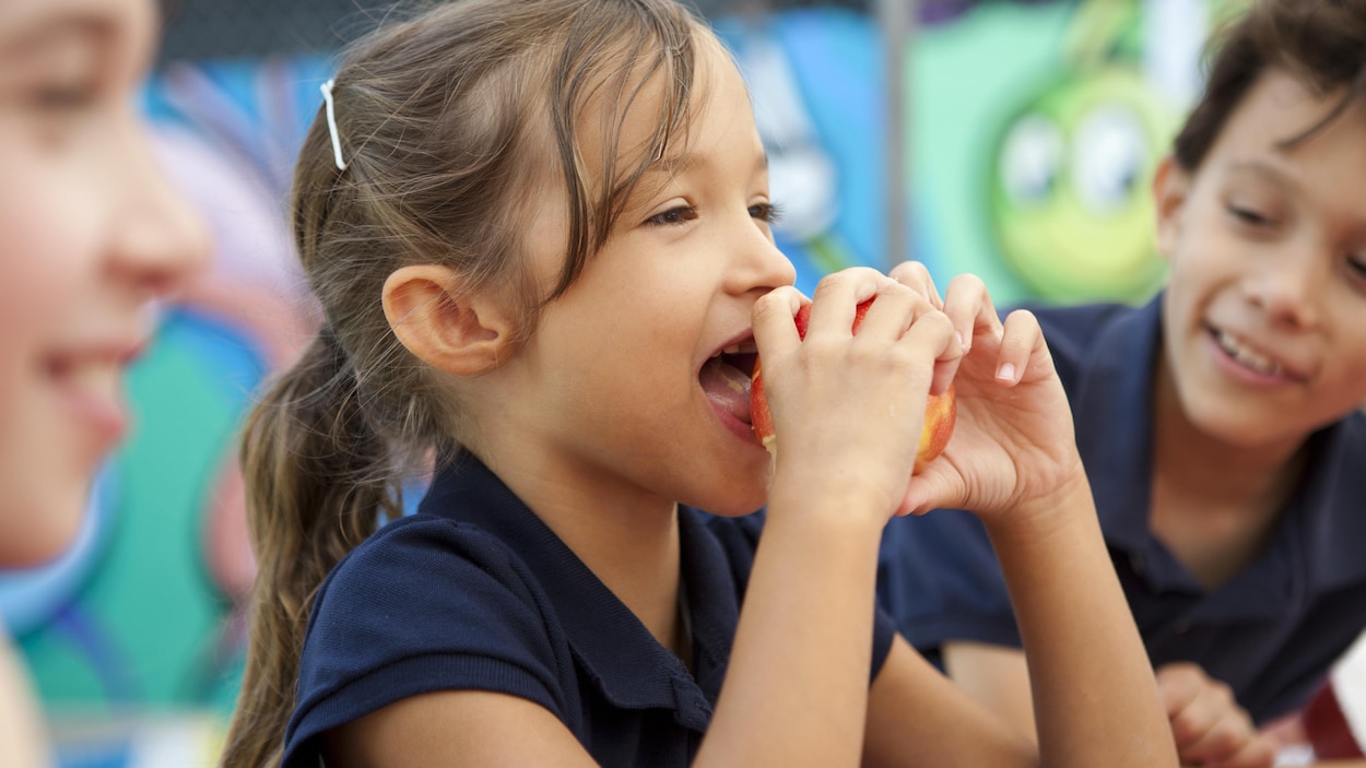 Une petite fille croque dans une pomme, entouré d'écoliers. Une petite fille croque dans une pomme, entouré d'écoliers.