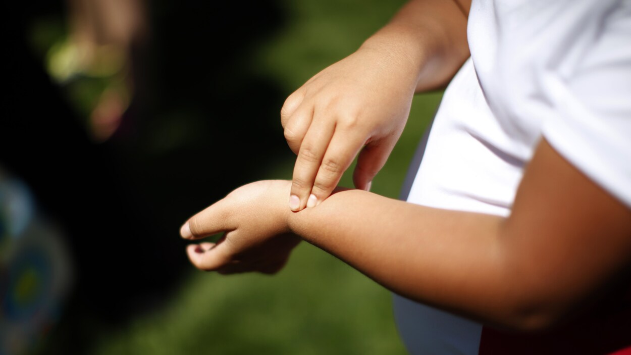 Un enfant, dont on ne voit que les bras et une partie de la poitrine, prend son pouls.