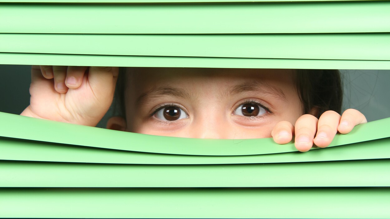 Un enfant regarde entre les lattes d'un store. Un enfant regarde entre les lattes d'un store.