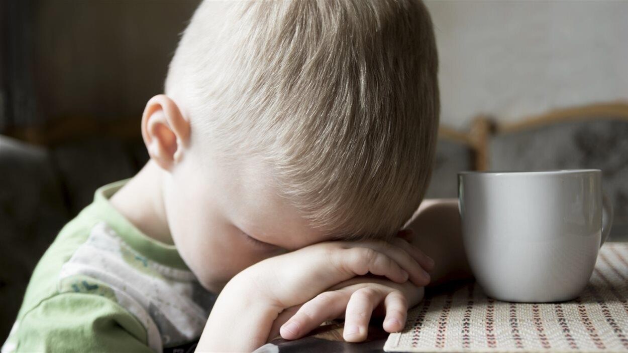 Un jeune garçon cache son visage avec ses mains.