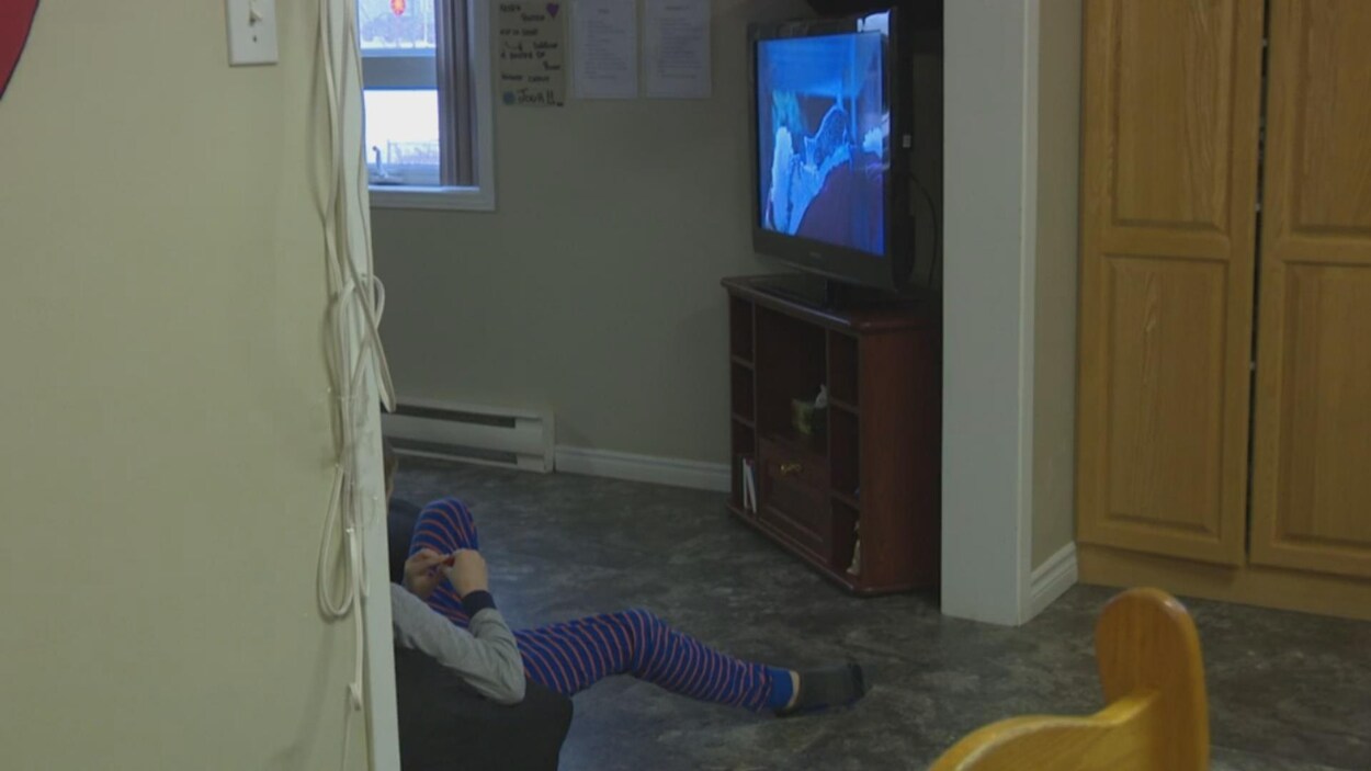 Un enfant assis contre un mur regarde la télévision.