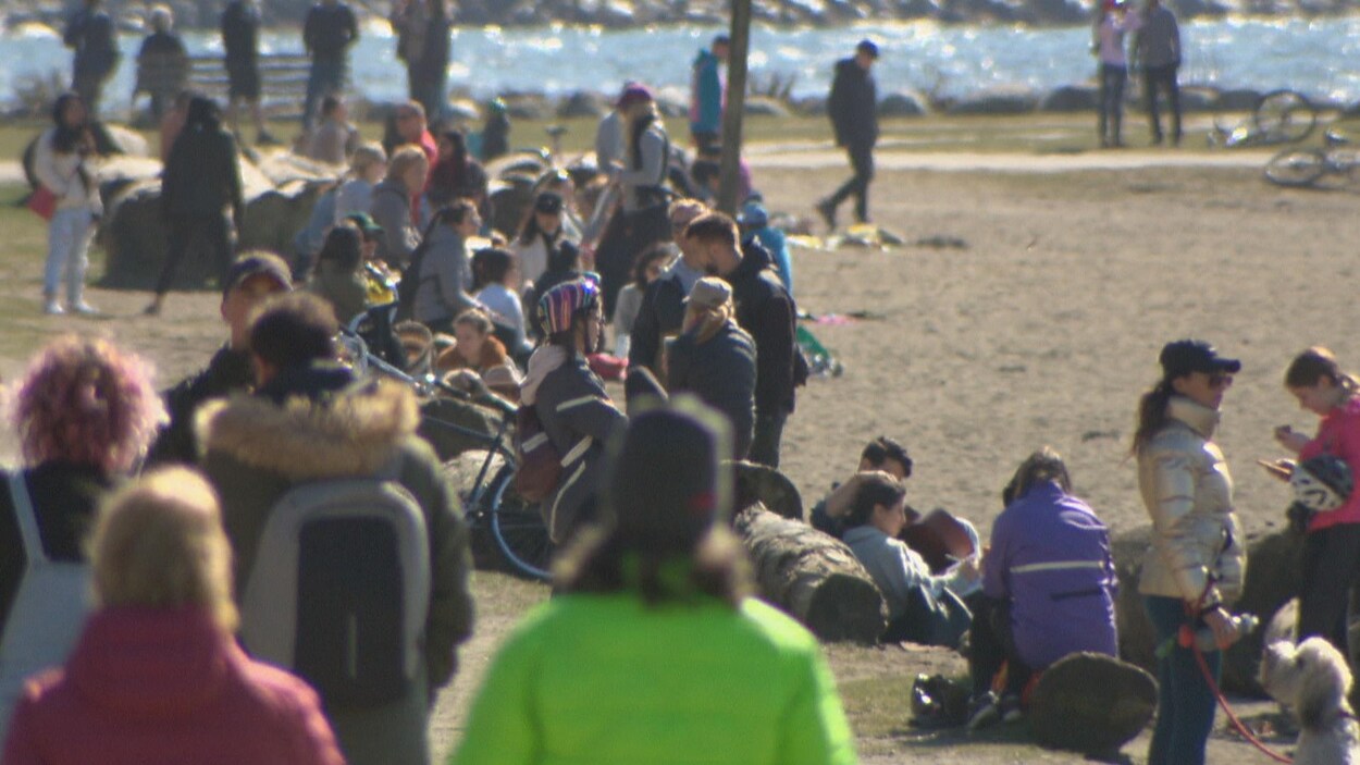 La plage d'English Bay est remplie de gens, dont certains sont rassemblés en groupe.
