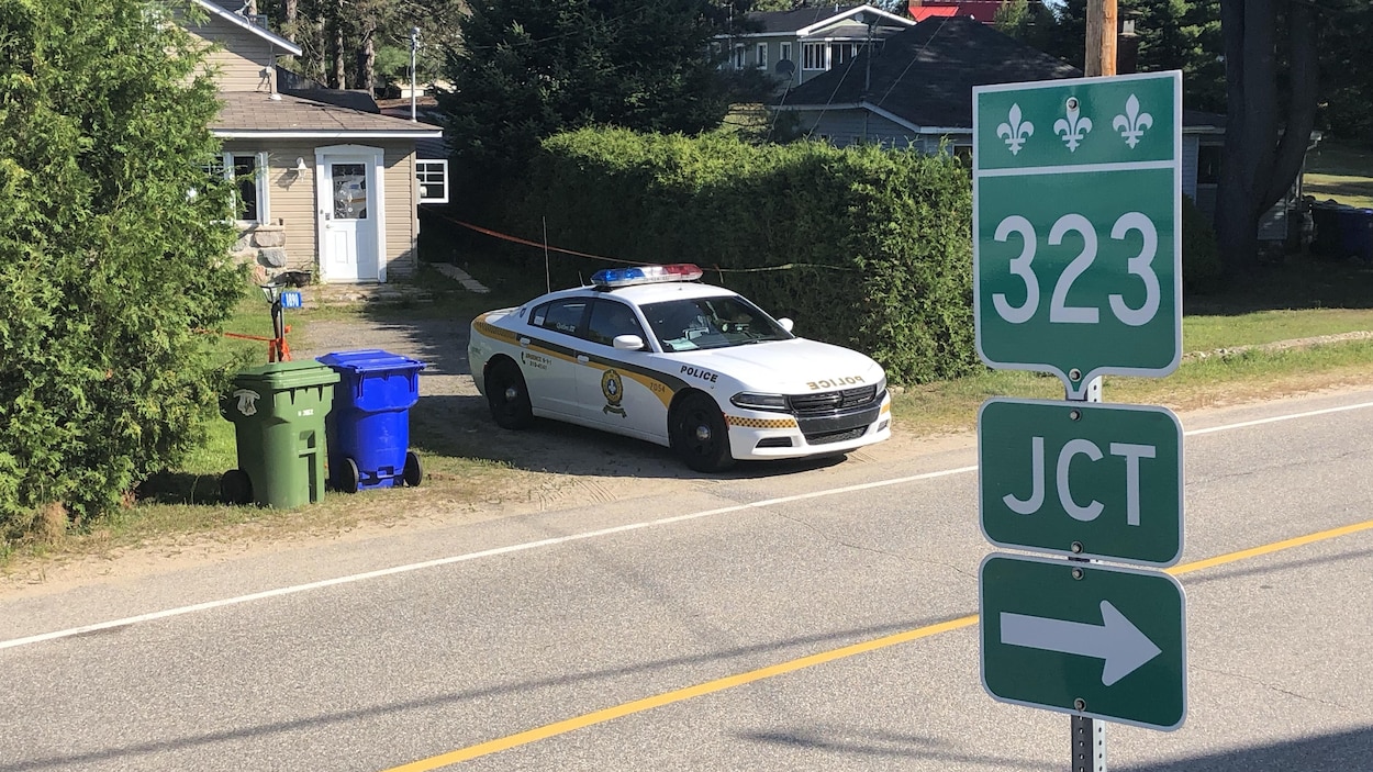 Une voiture de la SQ est stationnée dans l'entrée du chalet, le long de la route 323.