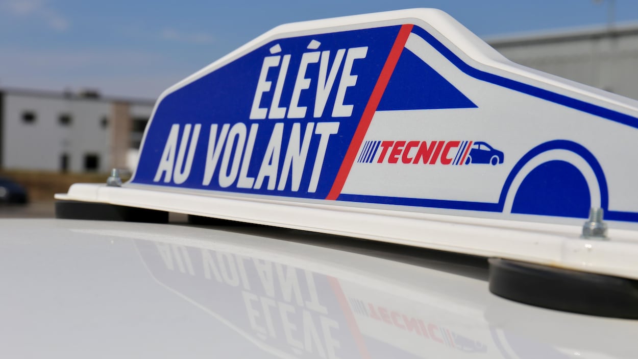 L’enseigne porte l’inscription « Élève au volant » peinte en lettres blanches sur fond bleu ainsi que le logo du Groupe Tecnic. L’enseigne porte l’inscription « Élève au volant » peinte en lettres blanches sur fond bleu ainsi que le logo du Groupe Tecnic.