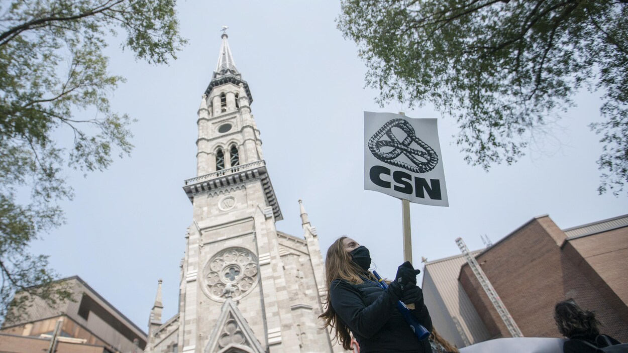 Une femme masquée brandit une pancarte portant le logo de la CSN.