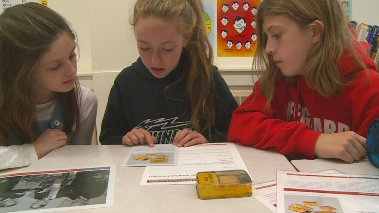 Trois jeunes élèves lisent un document dans une salle de classe.