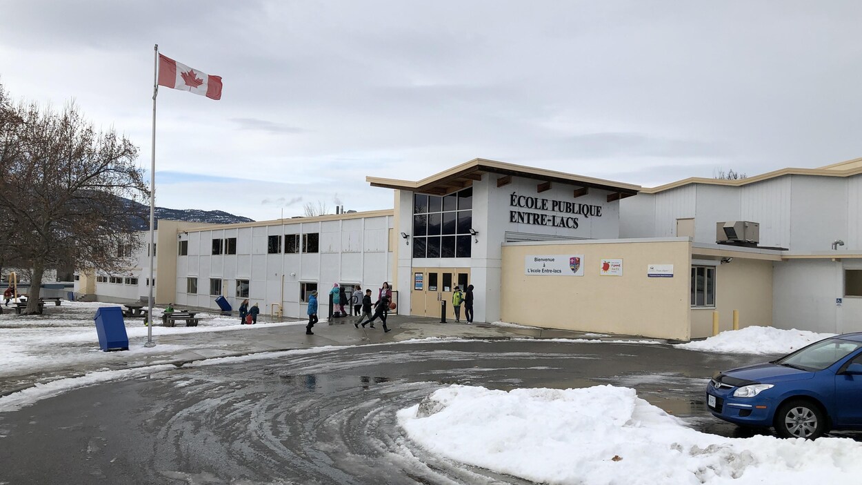 Plan large de la façade de l'école publique Entre-Lacs, on peut voir des élèves qui marchent vers la porte d'entrée de l'école.