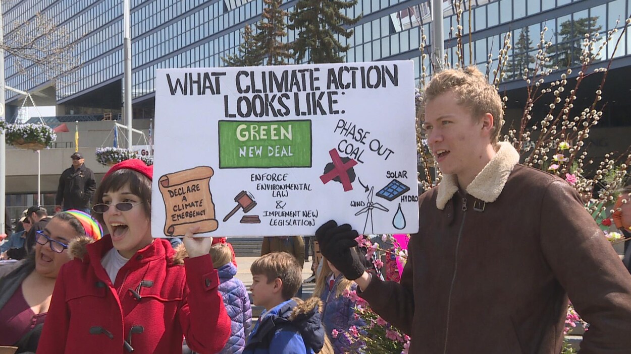 Deux jeunes adultes qui tiennent une pancarte dans leur main. Sur la pancarte, on peut voir des exemples d'actions pour sauver la planète, par exemple, favoriser les énergies renouvelables.