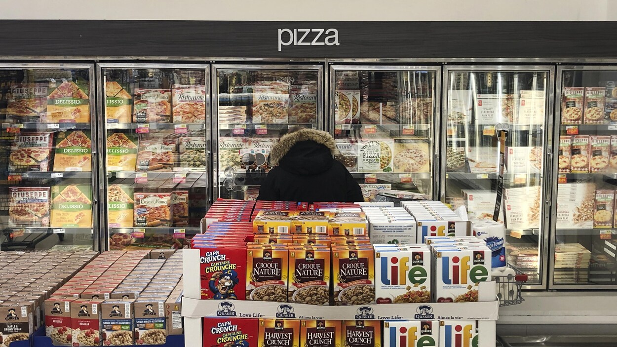 Un homme se trouve dans le rayon des pizzas surgelées dans une épicerie.
